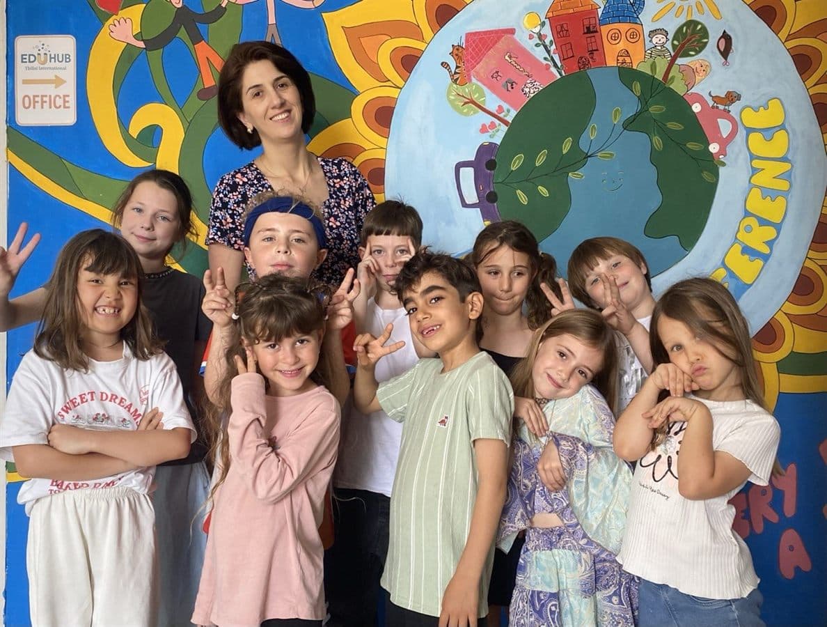EDUHUB Tbilisi group photo: children and their teacher in front of the painted wall mural