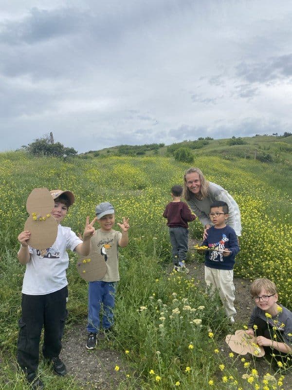 Children on an outdoor walk in a wildflower meadow with their craft cut-outs
